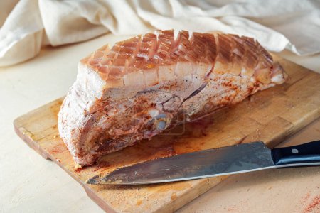 Photo for Raw piece of pork meat with fat rind rubbed with mustard and spices on a wooden kitchen board, ready prepared for the oven for a delicious crust roast, selected focus, narrow depth of field - Royalty Free Image