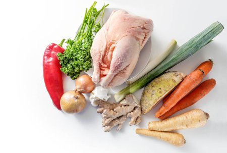 Photo for Raw ingredients for a healthy chicken broth against cold and flu with root vegetables, leek, ginger, onion, garlic and red bell pepper on a light background, high angle view from above, copy space - Royalty Free Image