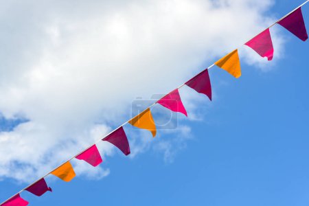 Foto de Los banderines en rosado, anaranjado y púrpura colgando diagonal en una línea contra un cielo azul y una nube blanca, decoración para un evento festivo de verano, espacio de copia - Imagen libre de derechos
