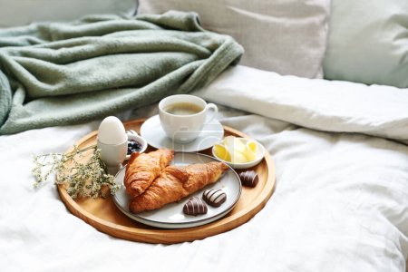 Muttertagsfrühstück mit Liebe im Bett serviert. Kaffee, Croissant, Ei und Schokoladenherzen auf einem Holztablett. Natürliche Bettdecke. Auch für Geburtstag, Valentinstag oder Vatertag, Kopierraum, ausgewählter Schwerpunkt