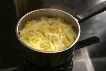 Nudeln werden in kochendem Wasser in einem Topf auf einer schwarzen Herdplatte gekocht, Essenszubereitung, Kopierraum, ausgewählter Fokus, enge Schärfentiefe