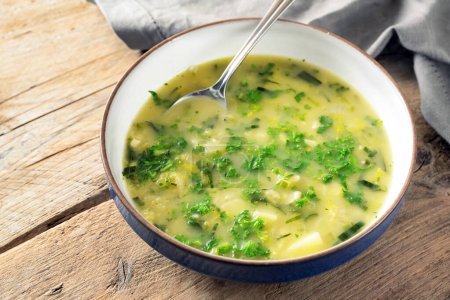 Potato parsley soup in a plate with spoon on a rustic wooden table, healthy vegetarian dish, copy space, selected focus, narrow depth of field