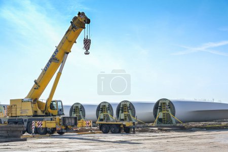 Photo for Rieps, Germany, April 22, 2023:  Wind turbine blades and a heavy industry crane stored near the construction site of a wind energy farm, installing a renewable power plant, copy space, selected focus - Royalty Free Image