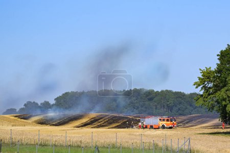 Photo for Fire engine and firefighters damping down a field fire to protect the surrounding area in a rural landscape, copy space, selected focus - Royalty Free Image
