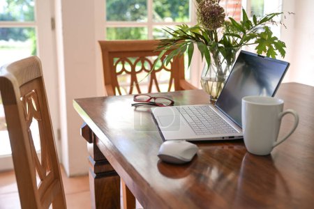 Téléchargez les photos : Ordinateur portable sur une table à manger en bois avec tasse à café et bouquet de fleurs dans le salon, concept de travail à domicile, espace de copie, mise au point sélectionnée, profondeur de champ étroite - en image libre de droit
