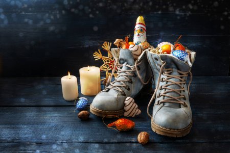 Téléchargez les photos : Tradition sur Nikolaus allemand Tag signification Nicholas jour, chaussures sont remplis de friandises, ici bottes avec des bonbons et décoration de Noël sur bois bleu foncé avec des bougies, espace de copie, foyer sélectionné - en image libre de droit