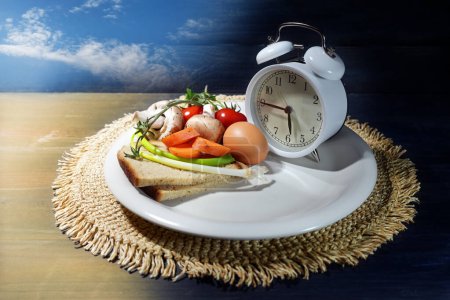 Intermittent fasting, plate with an alarm clock and partly filled with food, diet concept of interval eating in a time slot one third of the day, background from light to dark, copy space, selected focus 