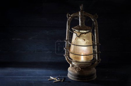 Photo for Rusty kerosene lantern shines undaunted with light in the dark, obsolete technology in times of modern energy-saving lamps, concept for tradition, hope or crisis prevention, copy space, selected focus - Royalty Free Image