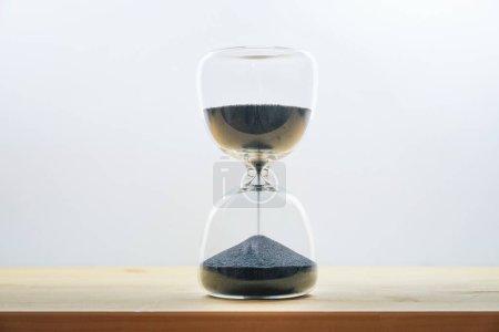 Hourglass with black sand on a wooden table against a light gray background, concept for time passing by, seize the day and enjoy the moment, copy space, selected focus