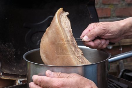 Cook takes a piece of slowly cooked rind meat out of the pot to make a stock sauce in a rustic kitchen, copy space, selected focus, narrow depth of field