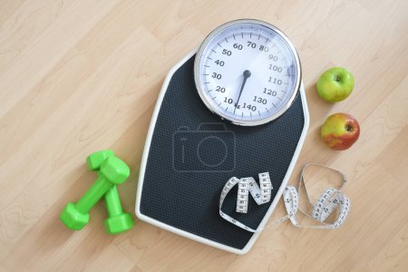 Fitness, diet and weight loss concept, personal scale with measuring tape, green dumbbells and two apples on a wooden floor, high angle view from above, copy space, selected focus