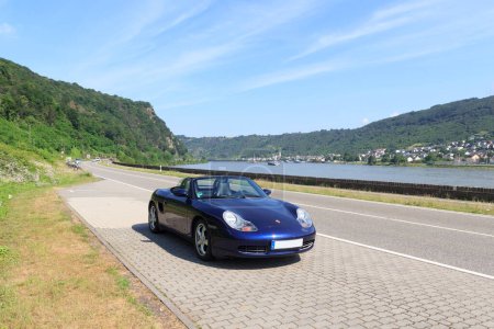 Foto de Boppard, Alemania - 26 de junio de 2021: Blue roadster Porsche Boxster 986 with river Rhine gorge panorama. El coche es un coche deportivo de dos plazas de motor medio fabricado por la empresa alemana Porsche. - Imagen libre de derechos