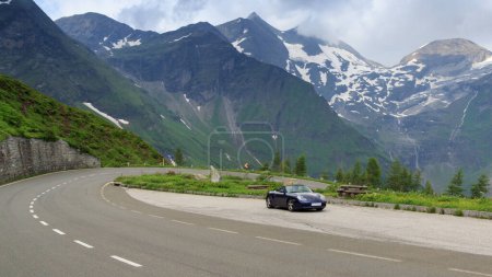 Foto de Fusch, Austria - 25 de julio de 2021: El roadster azul Porsche Boxster 986 con panorama de montaña y curva de horquilla en Grossglockner High Alpine Road. El coche es un coche deportivo fabricado por Porsche. - Imagen libre de derechos
