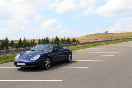 Foto de Gersfeld, Alemania - 23 de julio de 2021: Porche Boxster 986 azul con vista panorámica de Wasserkuppe y cúpula de radar en las montañas Rhoen. El coche es un coche deportivo de dos plazas de motor medio fabricado por Porsche. - Imagen libre de derechos