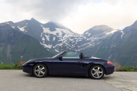 Foto de Fusch, Austria - July 25, 2021: Blue roadster Porsche Boxster 986 with mountain panorama at Grossglockner High Alpine Road. The car is a mid-engine two-seater sports car manufactured by Porsche. - Imagen libre de derechos