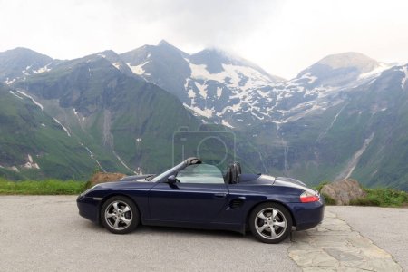 Foto de Fusch, Austria - July 25, 2021: Blue roadster Porsche Boxster 986 with mountain panorama at Grossglockner High Alpine Road. The car is a mid-engine two-seater sports car manufactured by Porsche. - Imagen libre de derechos