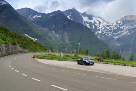 Photo for Fusch, Austria - July 25, 2021: Blue roadster Porsche Boxster 986 with mountain panorama and  hairpin curve at Grossglockner High Alpine Road. The car is a sports car manufactured by Porsche. - Royalty Free Image