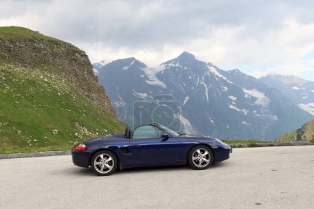 Photo for Fusch, Austria - July 25, 2021: Blue roadster Porsche Boxster 986 with mountain panorama at Grossglockner High Alpine Road. The car is a mid-engine two-seater sports car manufactured by Porsche. - Royalty Free Image