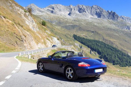 Foto de Realp, Suiza - 13 de agosto de 2022: Blue roadster Porsche Boxster 986 with mountain panorama at Furka Pass road. El coche es un coche deportivo de dos plazas de motor medio fabricado por Porsche. - Imagen libre de derechos