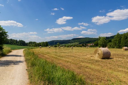 Rural scene with round hay bales, hill panorama and hiking path near village Wannbach in Franconian Switzerland, Germany