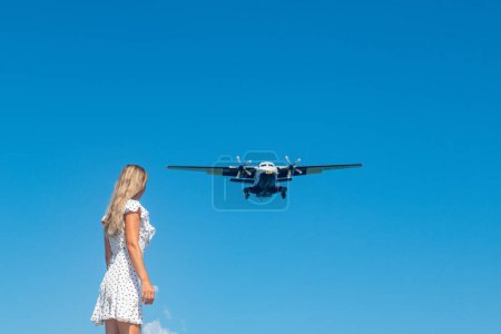 Photo for Coastal Encounter: Girl in White Dress on Stones, Plane in Blue Skies. High quality photo - Royalty Free Image