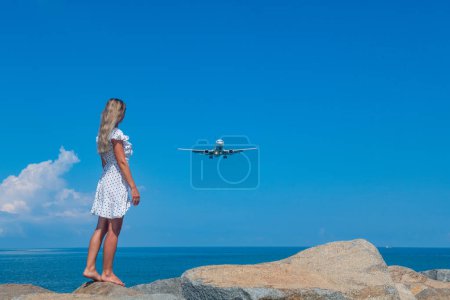 Photo for Seaside Serendipity: Girl in White Dress, Stones, Blue Sea and a Plane. High quality photo - Royalty Free Image