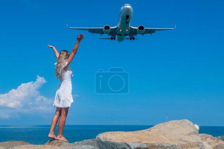 Photo for Oceanic Connection: A Girl in a White Dress on Stones Meets a Flying Plane. High quality photo - Royalty Free Image