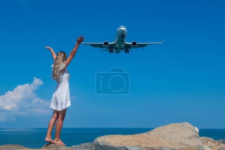 Photo for Aerial Rendezvous: Girl in White Dress on Stones, Plane Above the Blue Sea. High quality photo - Royalty Free Image