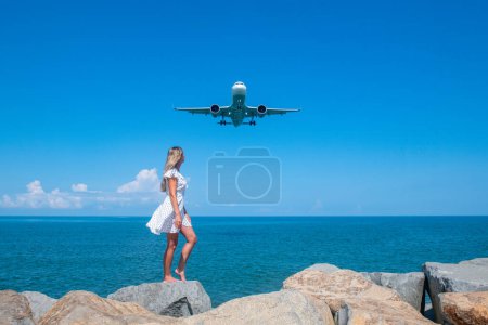 Mystische Union: Mädchen in weißem Kleid auf Steinen, Flugzeug wagt das blaue Meer. Hochwertiges Foto