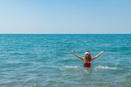 Photo for Santa Hat Splashdown: Girl in Red Swimsuit and Seaside. High quality photo - Royalty Free Image