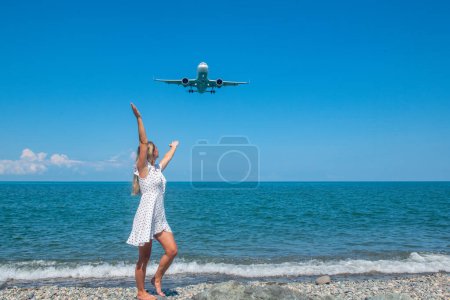 Photo for Parallel Journeys: Girl in White Dress on Stones, Plane Crossing the Blue Sea. High quality photo - Royalty Free Image
