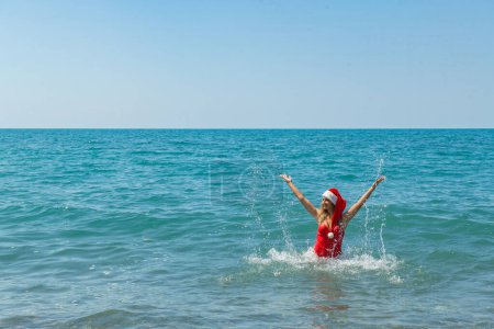 Photo for Coastal Santa Swim: Girl in Red Swimsuit and Festive Hat. High quality photo - Royalty Free Image