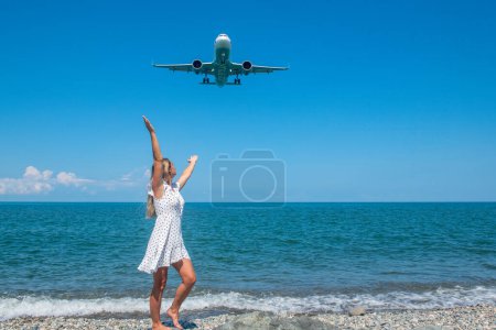 Seaside Escapade: Mädchen in weißem Kleid auf Steinen, Flugzeug, das das blaue Meer umarmt. Hochwertiges Foto
