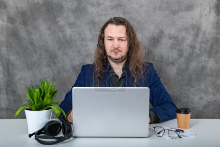A stylish and trendy man with long hair is posing in a blue suit, making different poses with a laptop and headphones. He exudes confidence and modernity, bringing a contemporary vibe to the image.