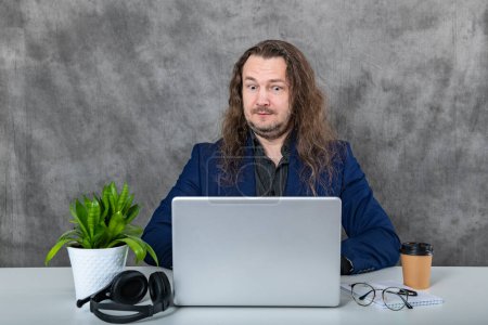 An elegant male model exudes confidence as he poses with a laptop, headphones, and trendy green flower glasses, all complementing his stylish blue suit in this high-fashion photo shoot.