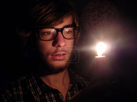 Téléchargez les photos : Dans l'obscurité, un homme trouve la lumière : regarder dans la flamme au milieu des ténèbres - en image libre de droit
