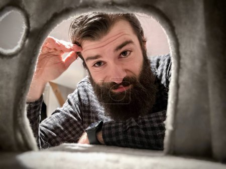Playful Perspective: Man Peering Through a Cardboard Cutout with a Curious Expression and Amused Smirk