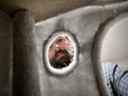 Verspielter Blick: Mann mit Bart durch ein Loch in Pappe, eine skurrile Perspektive