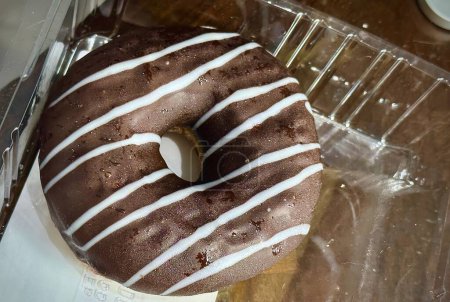 Tempting Chocolate Frosted Donut with White Icing Stripes, a Sweet Treat in a Clear Plastic Container