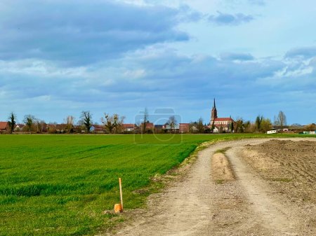 Photo for Rustic Trail Leading to a Quaint Village with a Stately Church in the Heart of Alsace's Countryside - Royalty Free Image