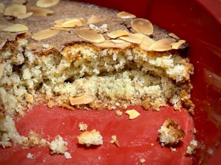Indulgence in a Bite: Close-Up of Moist Almond Cake Crumbs in a Red Ceramic Dish