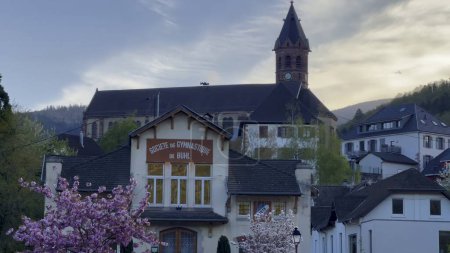 Crépuscule serein dans le village de Buhl avec des arbres en fleurs et clocher de l'église, Alsace, France, avec "Société de gymnastique Buhl" écrit sur la façade du bâtiment