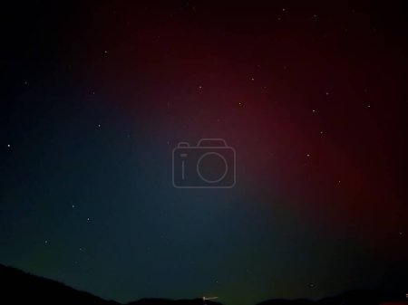 Subtle Red and Green Aurora Borealis Stretching Across the Starlit Sky Over a Mountainous Horizon in Europe, May 2024