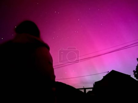Silhouettierter Beobachter unter einem spektakulären rosa Polarlicht in Frankreich während des Sonneneruptionsereignisses im Mai 2024