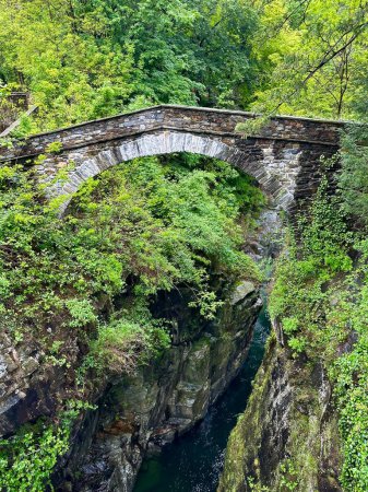 Antike steinerne Bogenbrücke über eine tiefe Schlucht, umgeben von üppigem Laub in Orrido di Sant 'Anna, Traffiume, Cannobio, Piemont, Italien, ein Zeugnis historischer Architektur