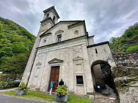 Foto de Cannobio, Italia - 7 de mayo de 2024: Fachada frontal de la iglesia histórica de Orrido di Sant 'Anna, con un campanario distintivo y enclavado en un entorno exuberante, Traffiume, Piemont - Imagen libre de derechos