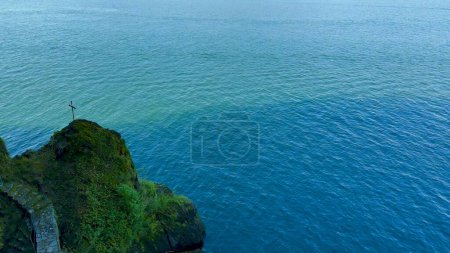 Scenic Aerial View of a Secluded Cliff with a Cross Overlooking the Calm Blue Ocean