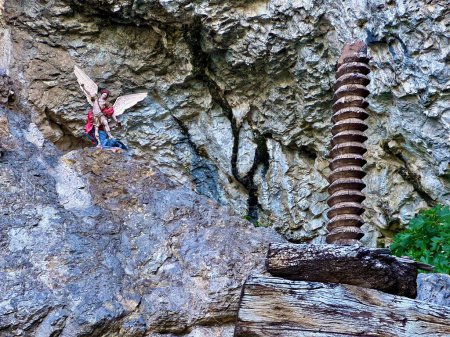 Escultura de roca al aire libre con figura angelical y tornillo de madera grande contra el fondo rocoso del acantilado