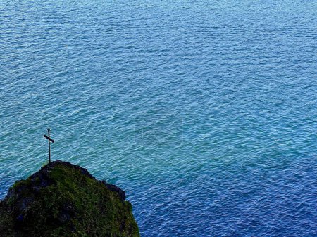 Croix solitaire sur une falaise couverte de mousse surplombant les eaux calmes de l'océan bleu