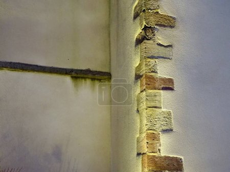 Nahaufnahme von freigelegtem Mauerwerk in einer alten Mauer mit strukturiertem Stuck und Umgebungsbeleuchtung